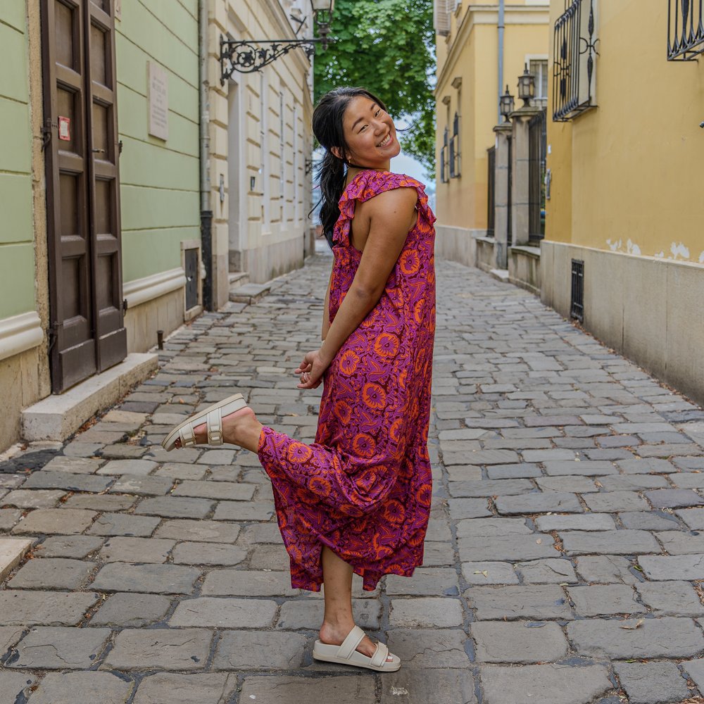 Lillian smiling and kicking up a leg on a cobblestone street